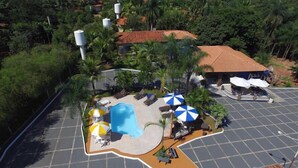 An aerial view of a resort with a swimming pool, lounge chairs, umbrellas, and a parking area. - Pousada Recanto Solar dos Passaros (Olímpia)