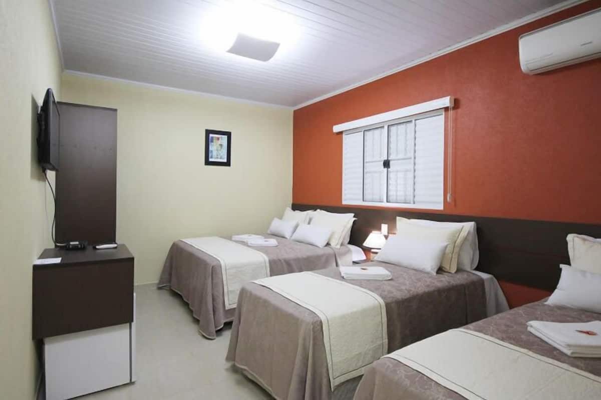 A hotel room with two beds, a TV, a desk, and a window with blinds.