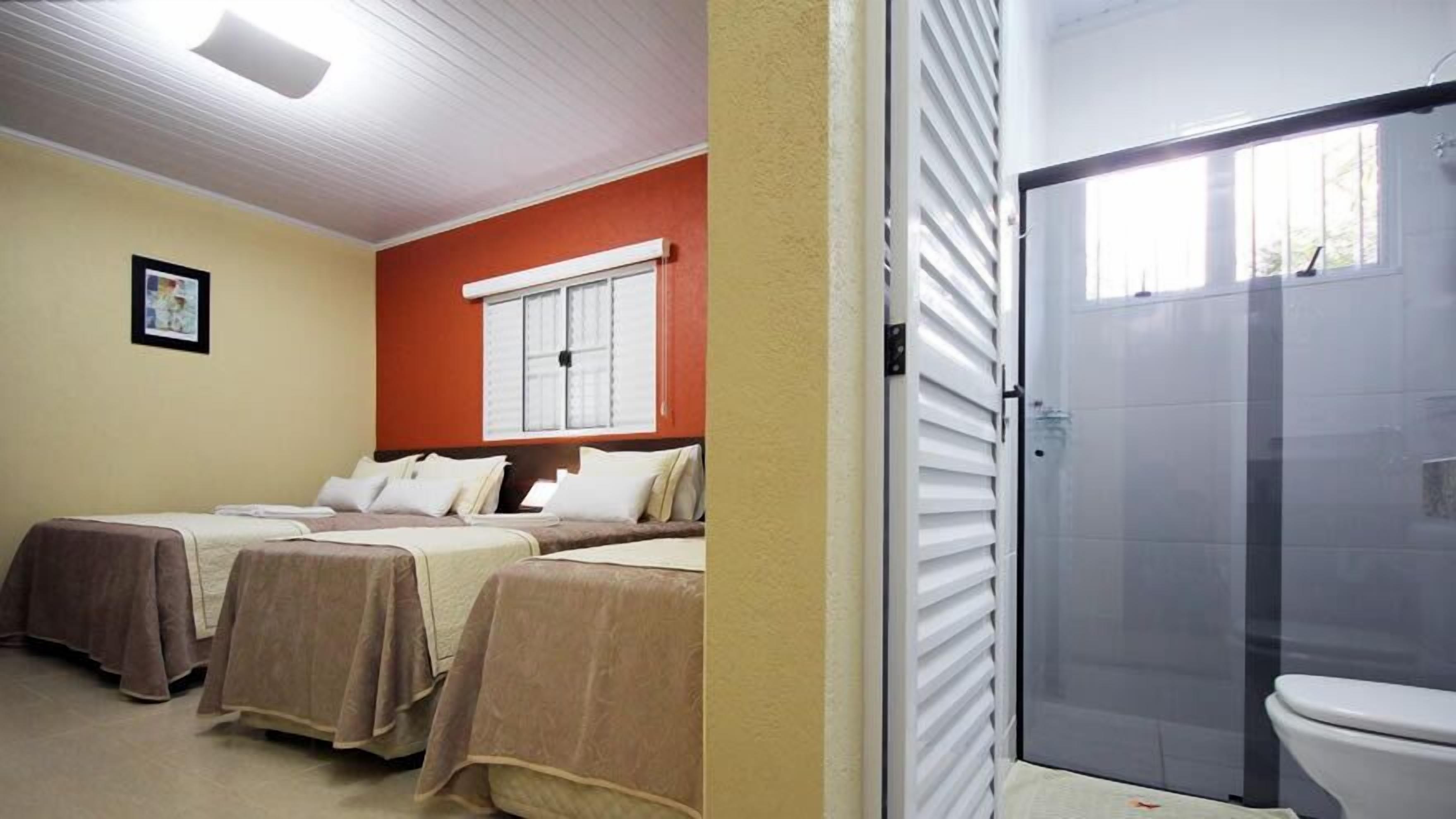 A hotel room with two beds, a window with shutters, and a shower area.