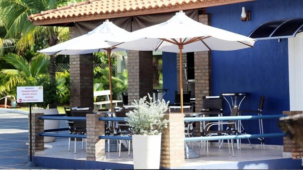An outdoor seating area with tables and chairs, umbrellas, and a sign indicating a private entrance. - Pousada Recanto Solar dos Passaros (Olímpia)