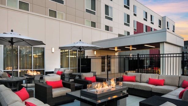 An outdoor seating area with sofas, tables, and umbrellas, featuring a central fire feature.