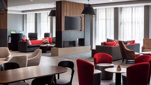 A modern hotel lobby with a fireplace, comfortable seating, and a large TV screen.
