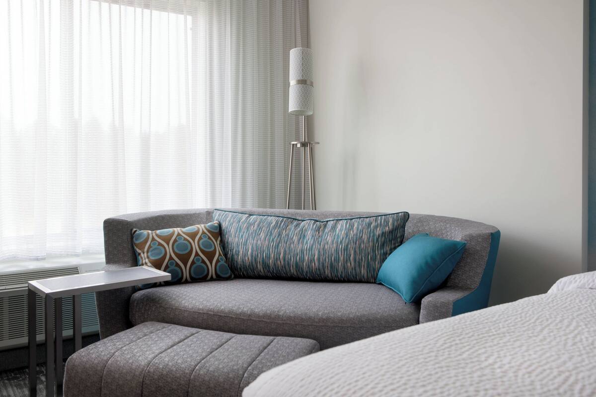 A modern hotel room with a grey sofa, a small table, and a floor lamp.