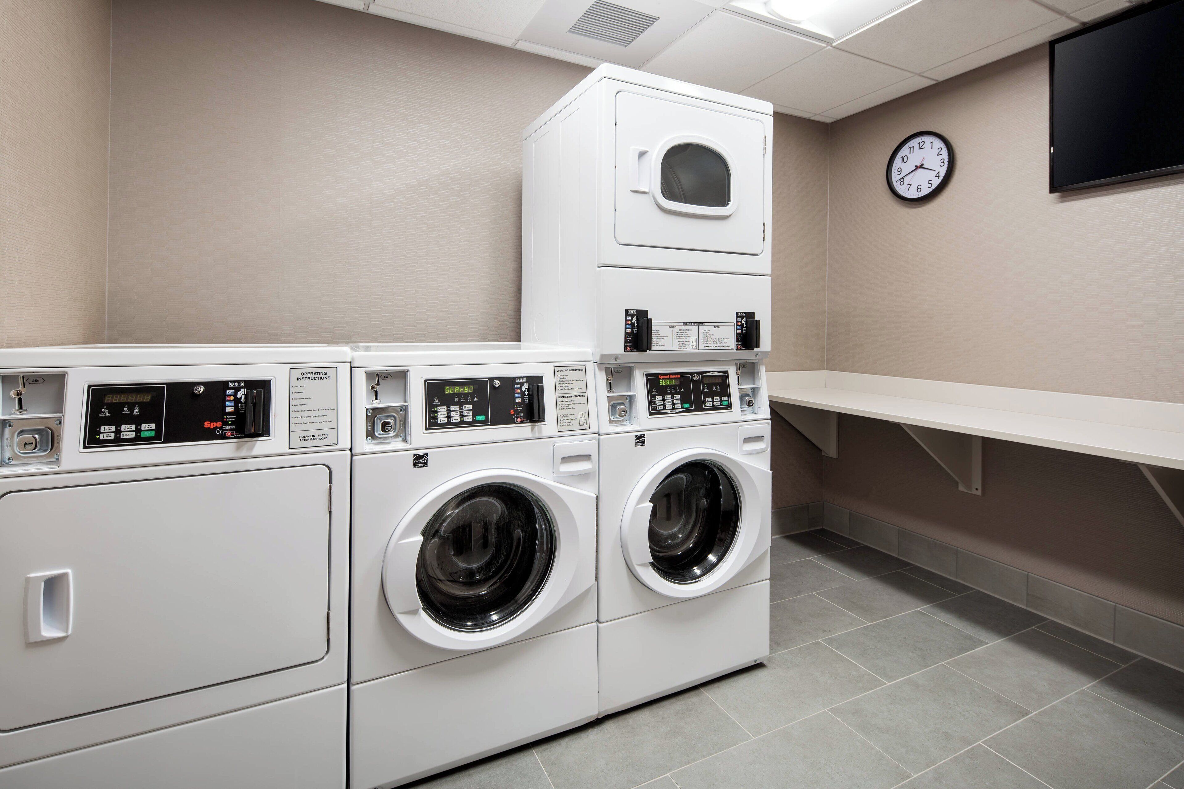 A laundry room with two front-loading washing machines, a dryer, and a clock on the wall.
