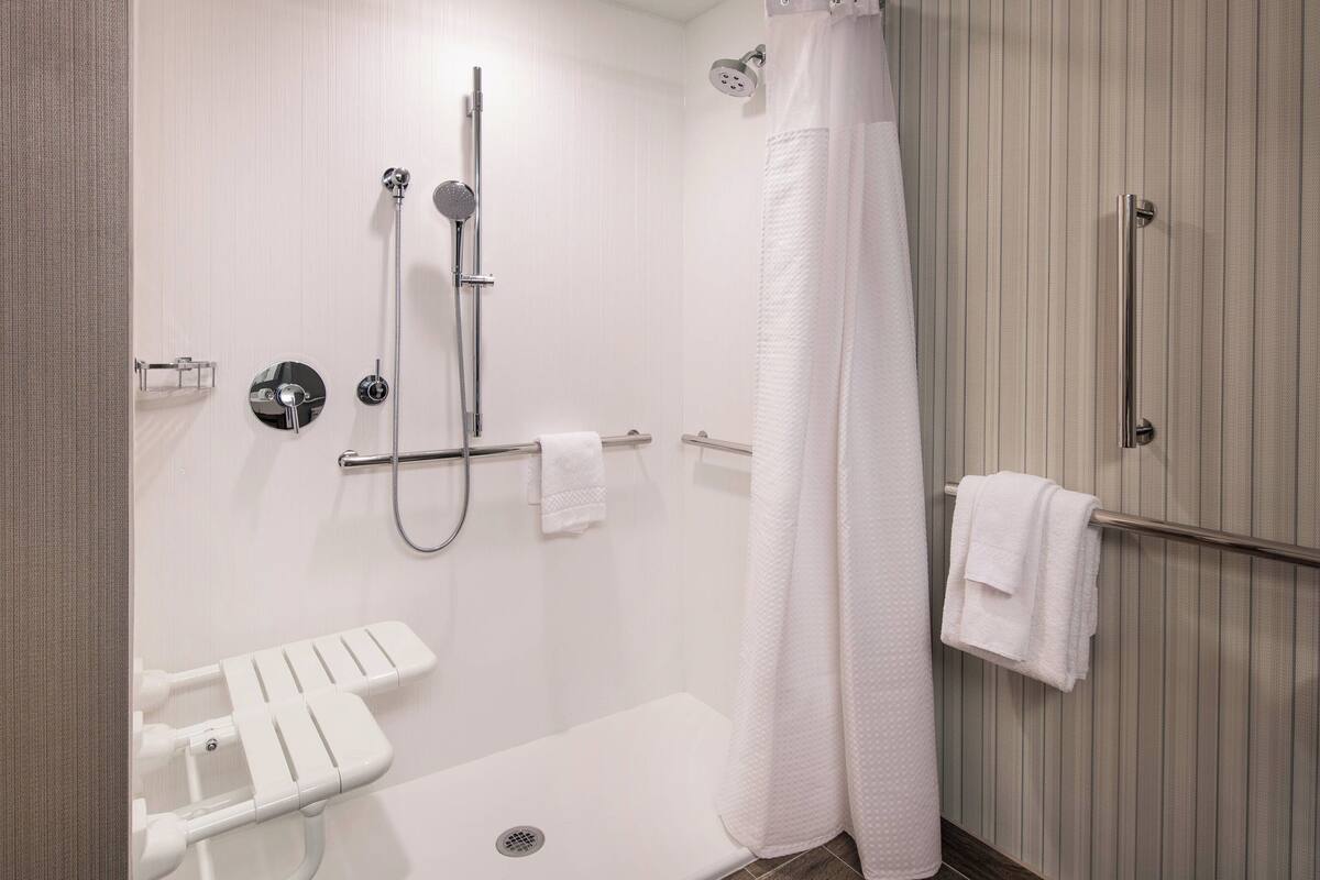 A modern bathroom with a shower, toilet, and handrails.