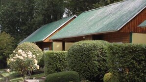 A row of wooden cabins with green roofs, surrounded by well-maintained hedges and a bench. - Los Charitos (El Calafate)