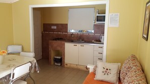 A compact kitchen with a microwave, sink, and cabinets. There is a dining table with chairs and a sofa with a floral cushion. - Los Charitos (El Calafate)
