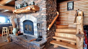 Un interior rústico con chimenea de piedra, escalones de madera y barandilla de madera.