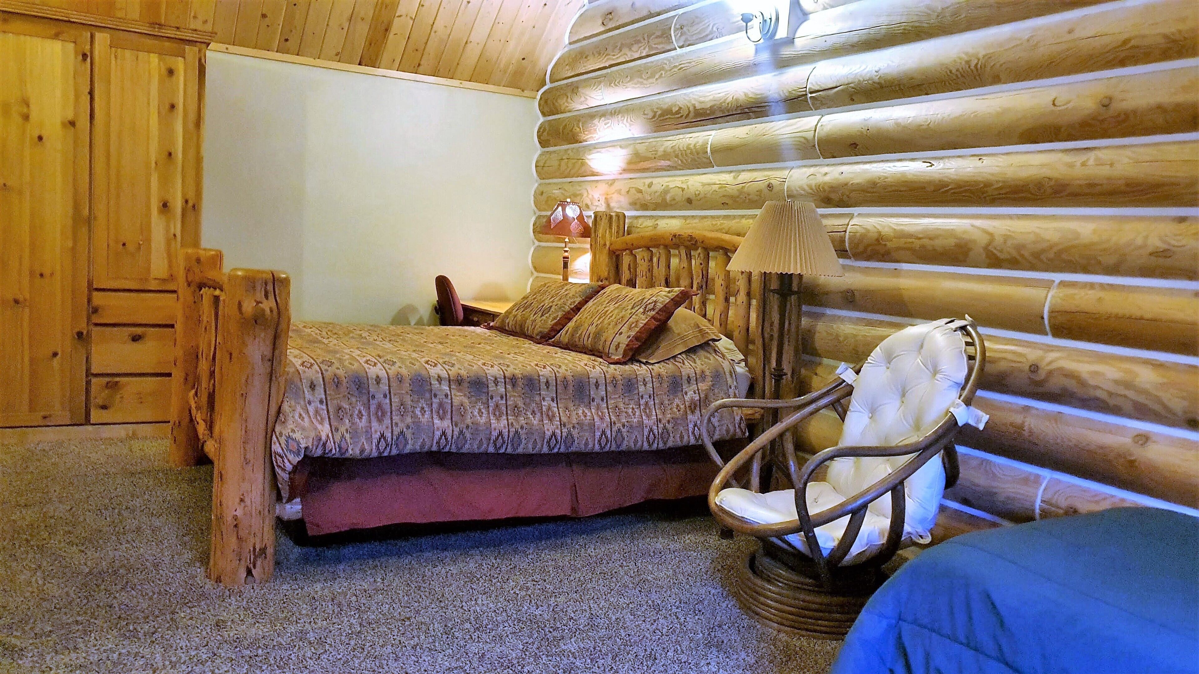 A log cabin room with a bed, a chair, and a lamp.