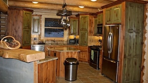 Una cocina con armarios de madera, un refrigerador de acero inoxidable, un microondas e isla de madera con un bote de basura.