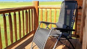 Una terraza de madera con una silla plegable de metal y barandilla de madera.