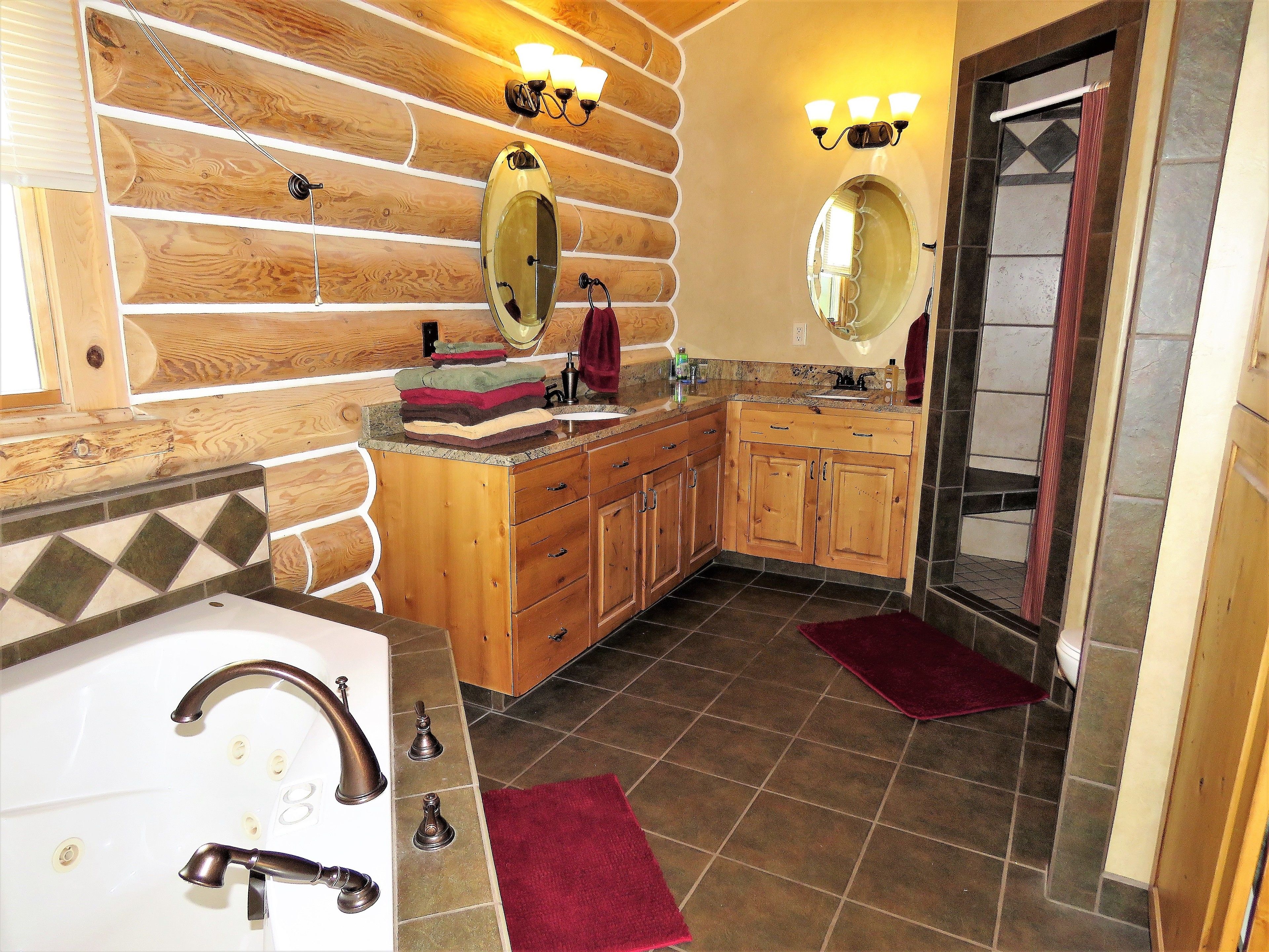 A bathroom with wooden cabinetry, a sink with a vanity, two mirrors, and a shower area.