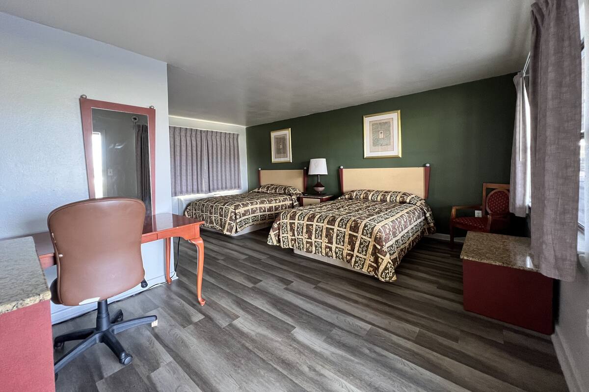 Ein Hotelzimmer mit zwei Betten, einem Schreibtisch, einem Stuhl und einem Vorhangfenster.