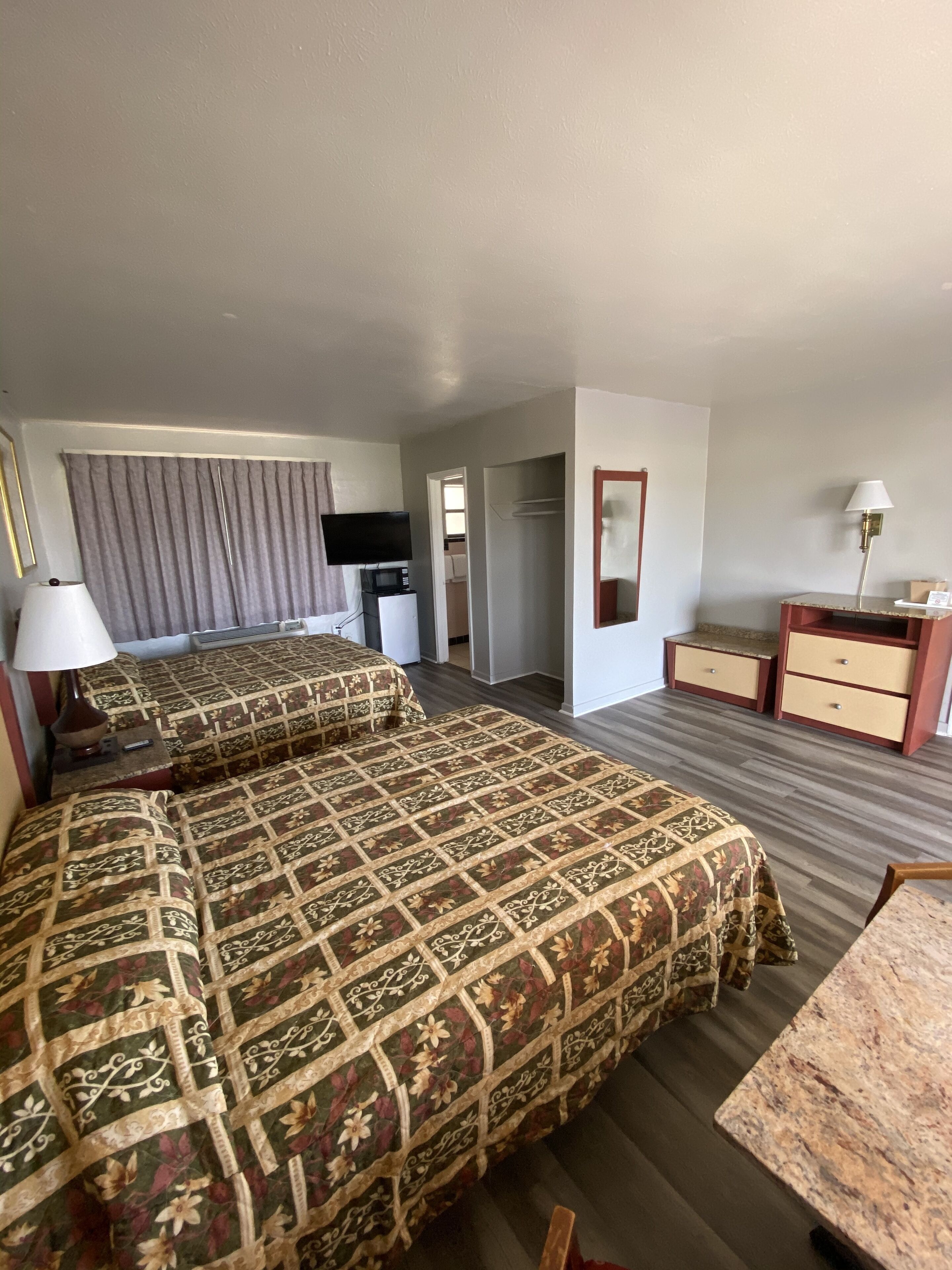 Ein Hotelzimmer mit zwei Betten, einem Schreibtisch, einem Stuhl, einem Fernseher, einer Lampe und einem Kleiderschrank.
