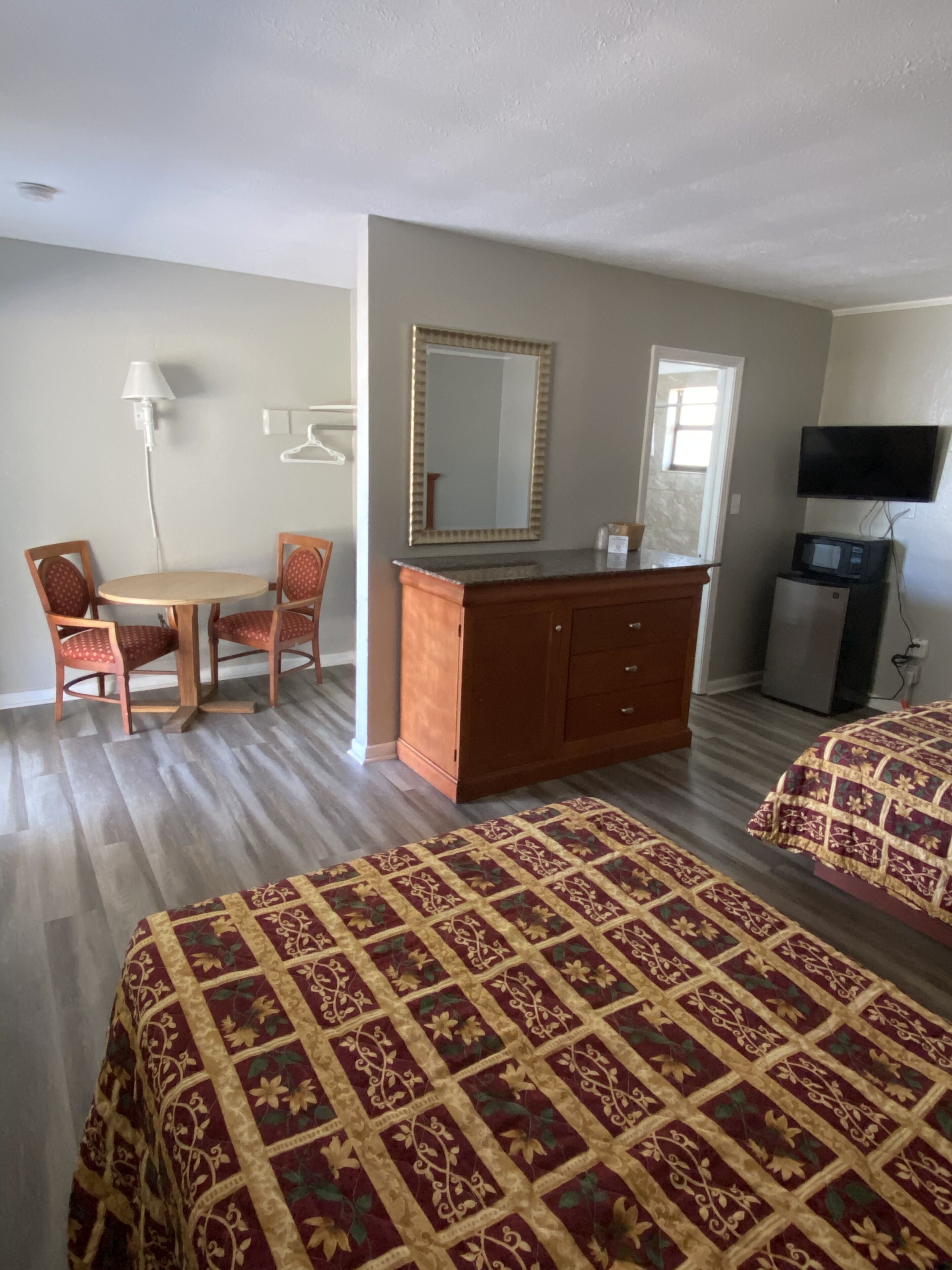 A hotel room with two beds, a wooden dresser, a desk with a chair, a television, and a microwave.