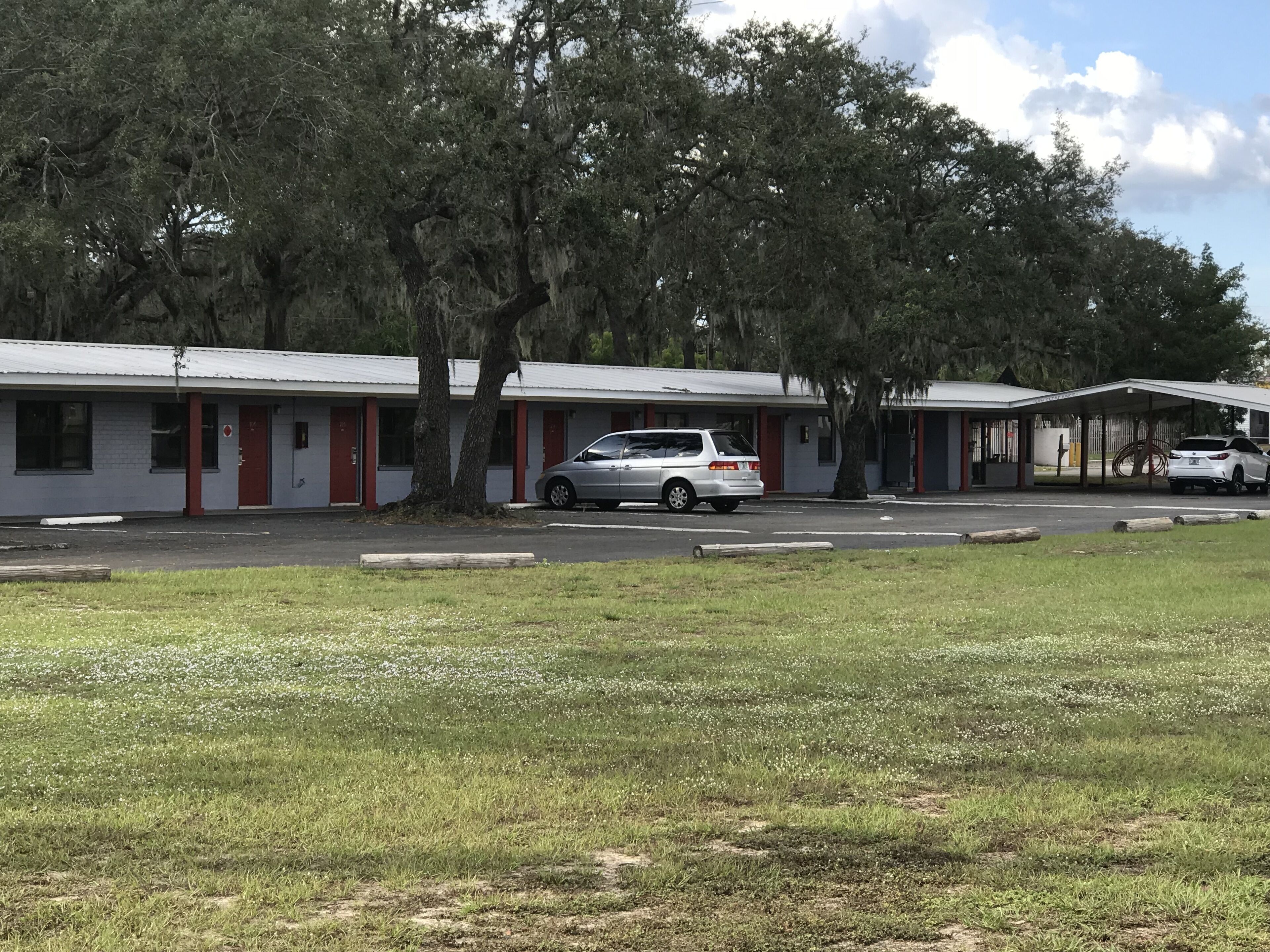 Um motel com edifícios de dois andares, cada um com uma porta vermelha e área de estacionamento coberta.