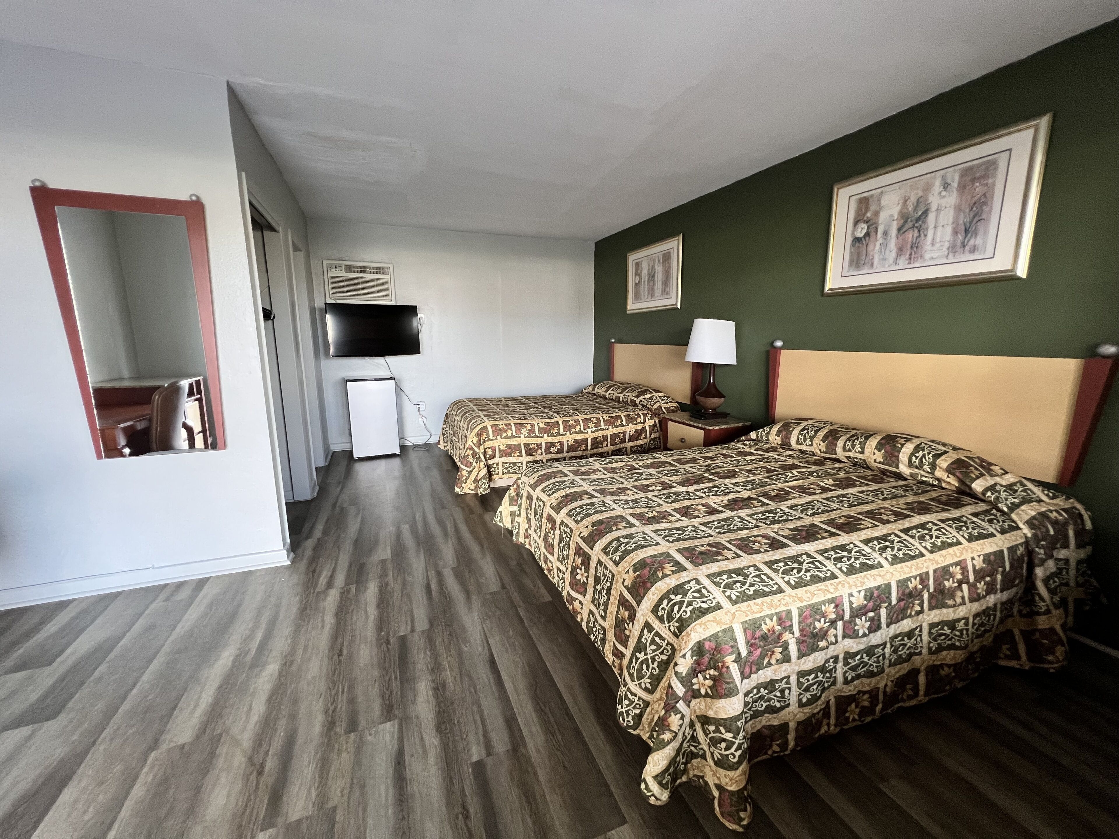 A hotel room with two beds, a television, a small refrigerator, and a mirror.