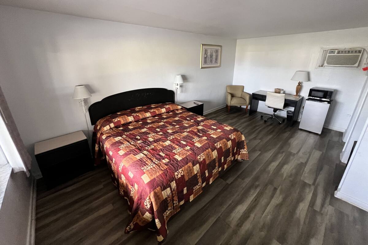 Ein Hotelzimmer mit Bett, Schreibtisch, Stuhl, Kühlschrank und Lampe.