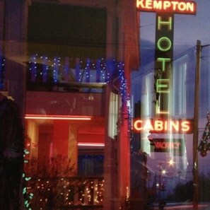 Un hotel llamado Kempton con letreros de neón, una entrada visible y un balcón con luces de cuerda.