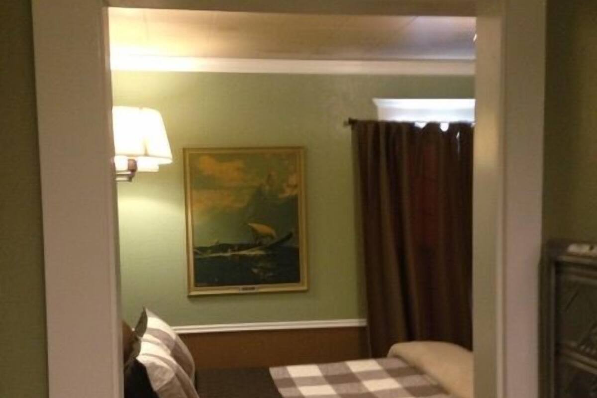 A hotel room with a checkered bedspread, a painting on the wall, and a lamp.