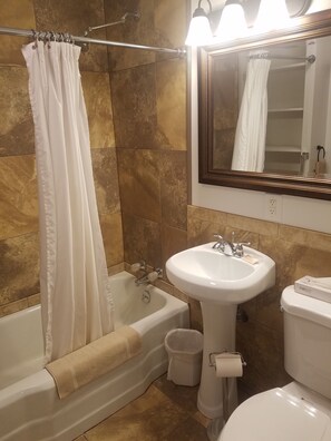 Un baño con bañera, lavamanos, inodoro y espejo.