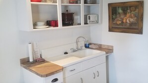 Una cocina con gabinetes blancos, encimera de madera, un lavamanos y un cubo de basura.