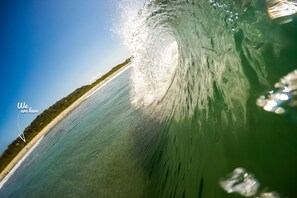 A wave in the ocean with a clear sky and a beach in the background. - Moana Surf Resort (Nosara)