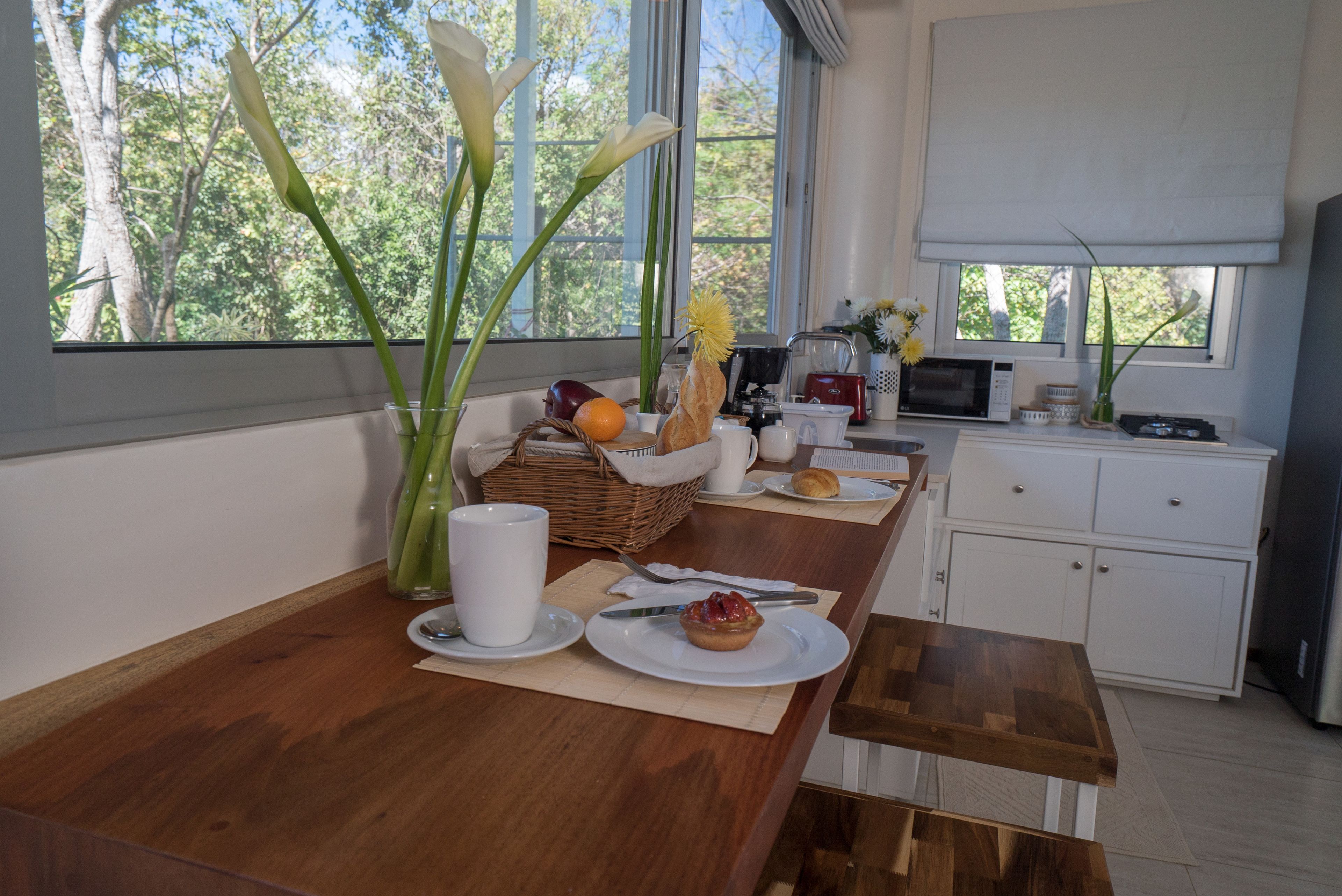 A kitchen with a wooden countertop, a microwave, a sink, and a window with a view of trees.