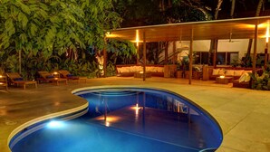 Area piscina con lettini e una zona relax coperta, circondata da vegetazione lussureggiante.