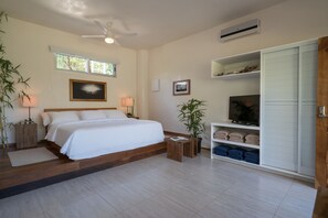 A bedroom with a bed, bedside tables, a TV, a wardrobe, and a ceiling fan. - Moana Surf Resort (Nosara)