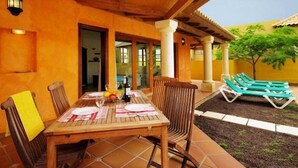 Un espacio de comedor al aire libre con mesa y sillas de madera, un pequeño jardín y una zona de descanso junto a la piscina.