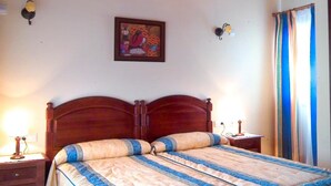 Un dormitorio con techo de madera, una cama con colcha, mesitas de noche y un cuadro enmarcado en la pared.
