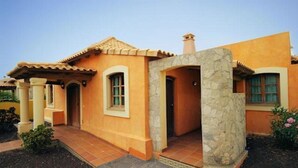 Una casa de dos pisos con fachada de estuco, techo de tejas y un pilar de piedra en la entrada.