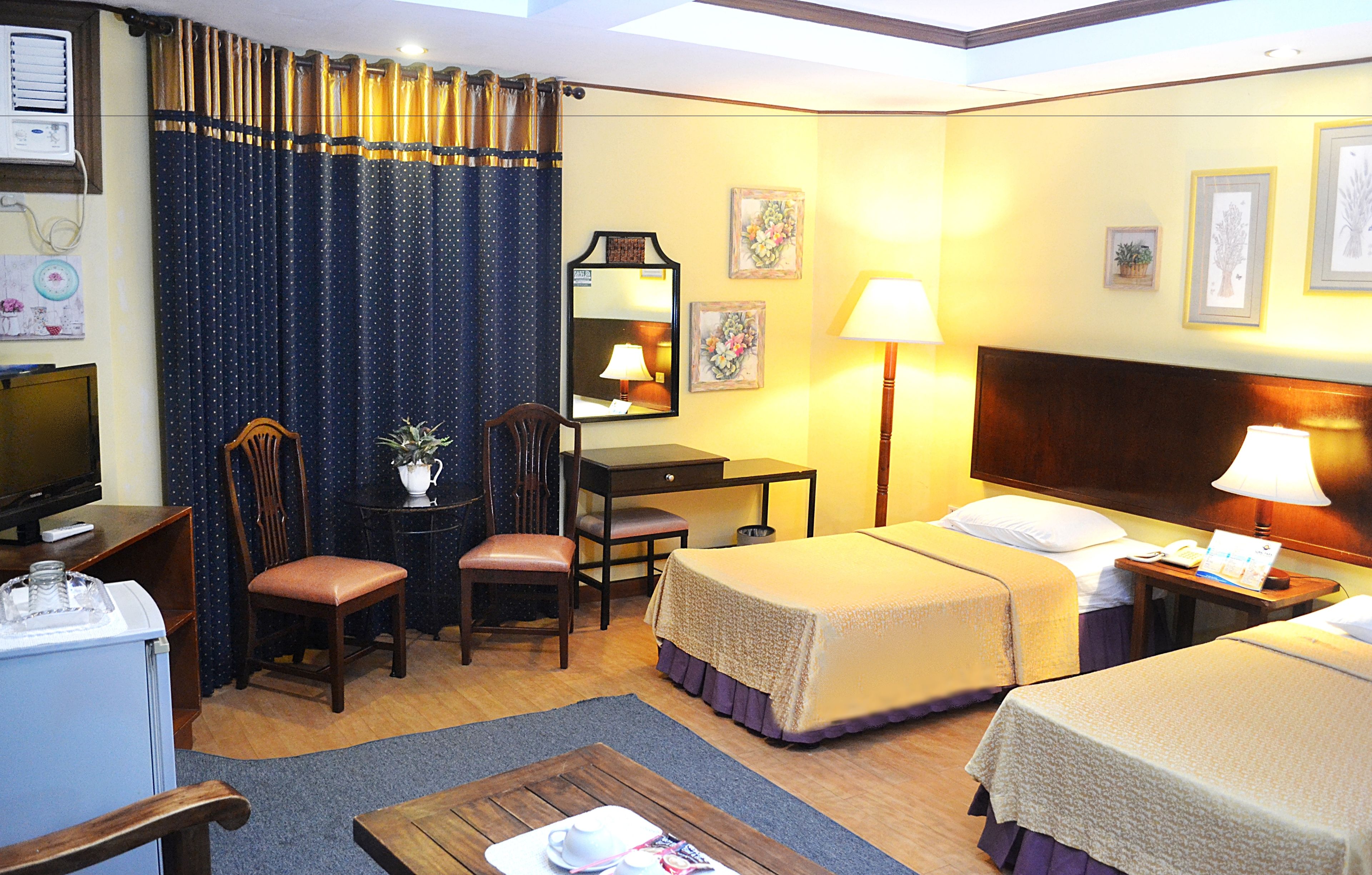 Une chambre d’hôtel avec deux lits, un bureau, une chaise, une télévision et une lampe.
