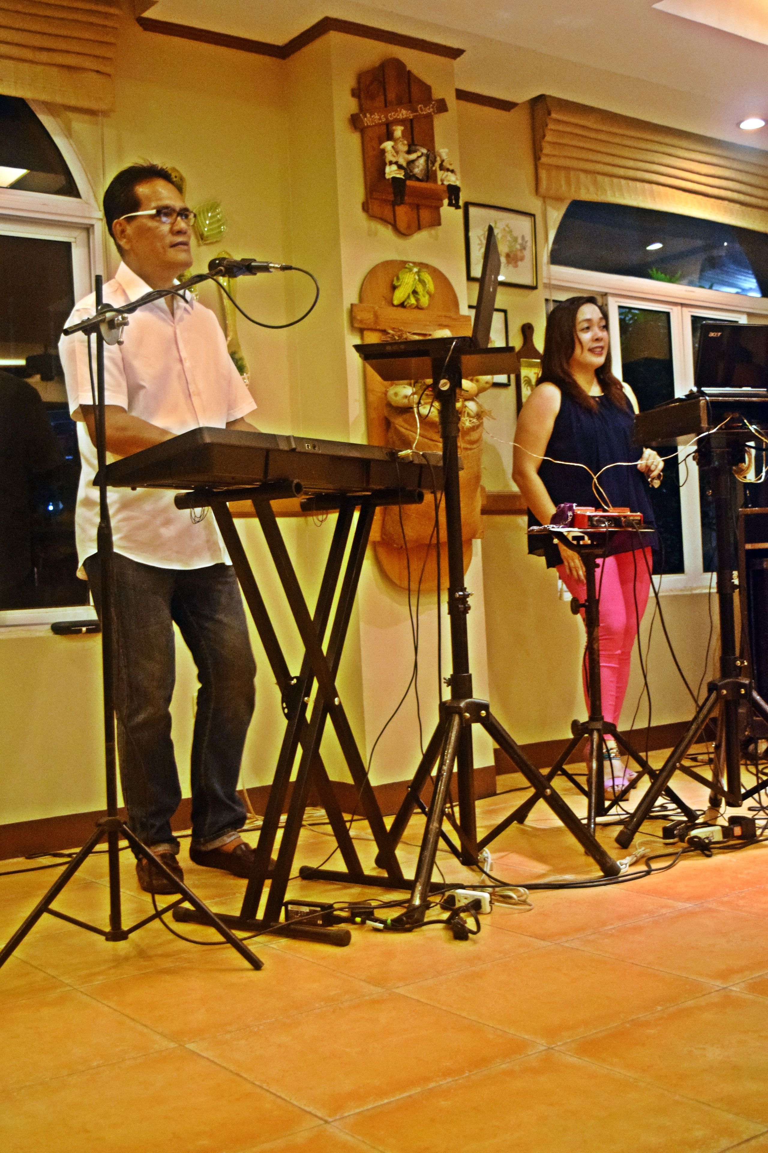 A man and a woman standing at a music stand with a keyboard and a microphone.