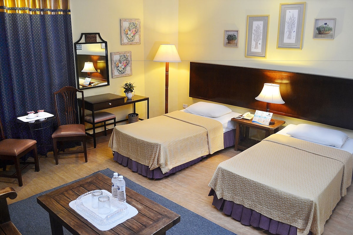 Habitación de hotel con dos camas, un escritorio, una silla, una mesa con bandeja y una lámpara.