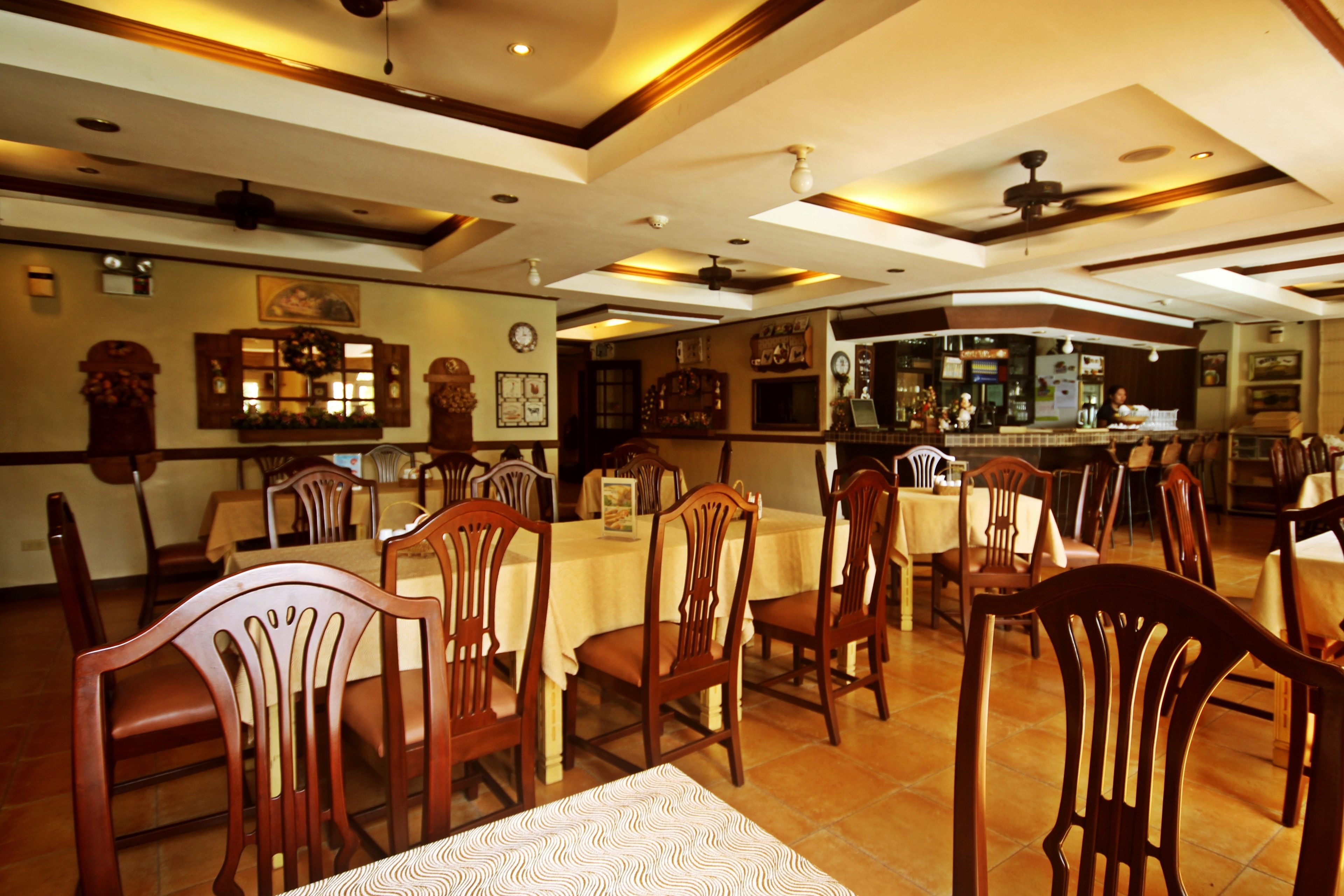 A restaurant with wooden chairs and tables, a bar area, and a ceiling fan.