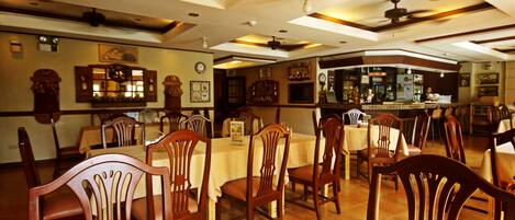 A restaurant with wooden chairs and tables, a bar area, and a ceiling fan.