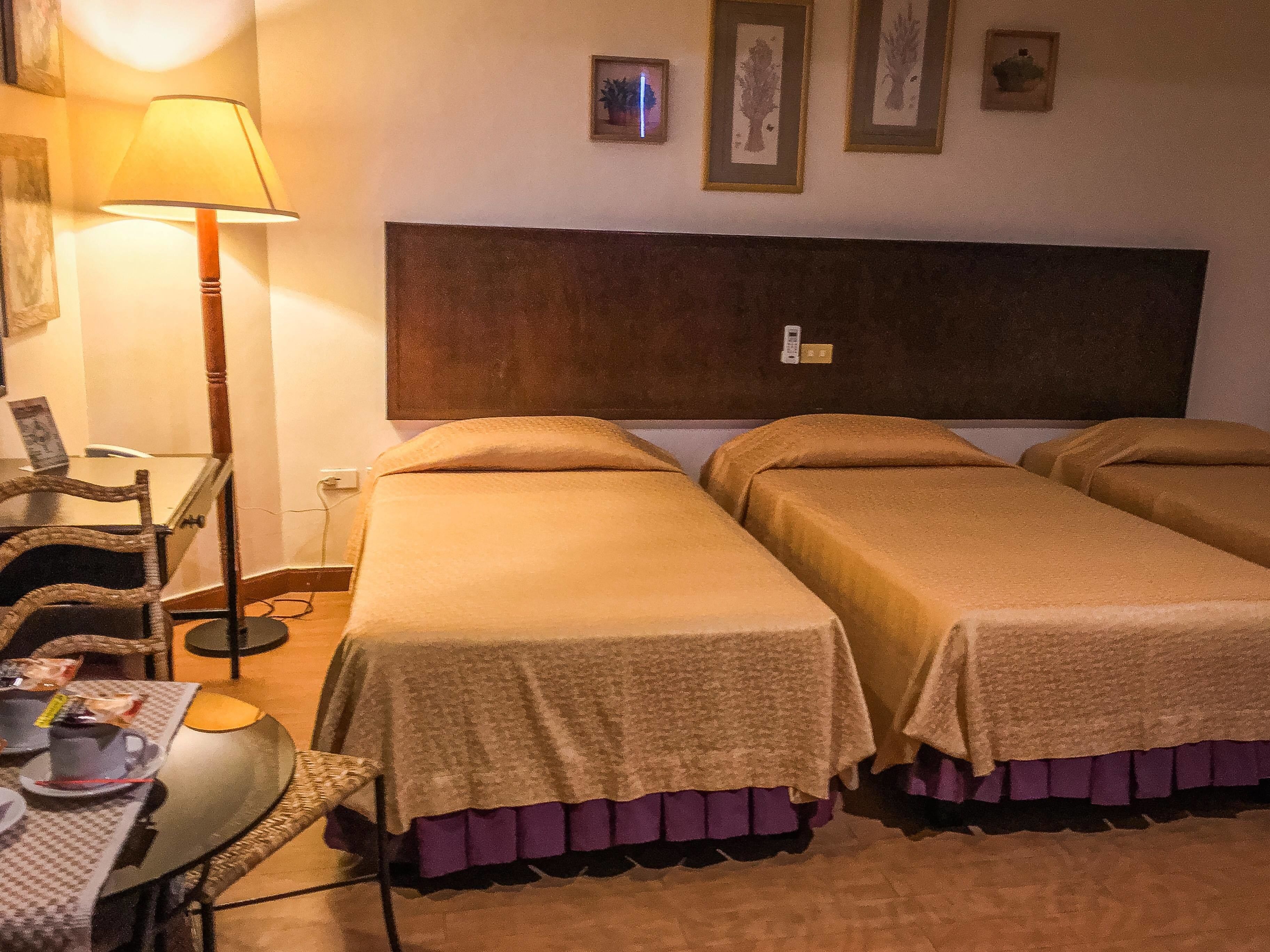 Une chambre d’hôtel avec deux lits simples, une petite table avec une chaise, une lampe et un téléphone fixé au mur.