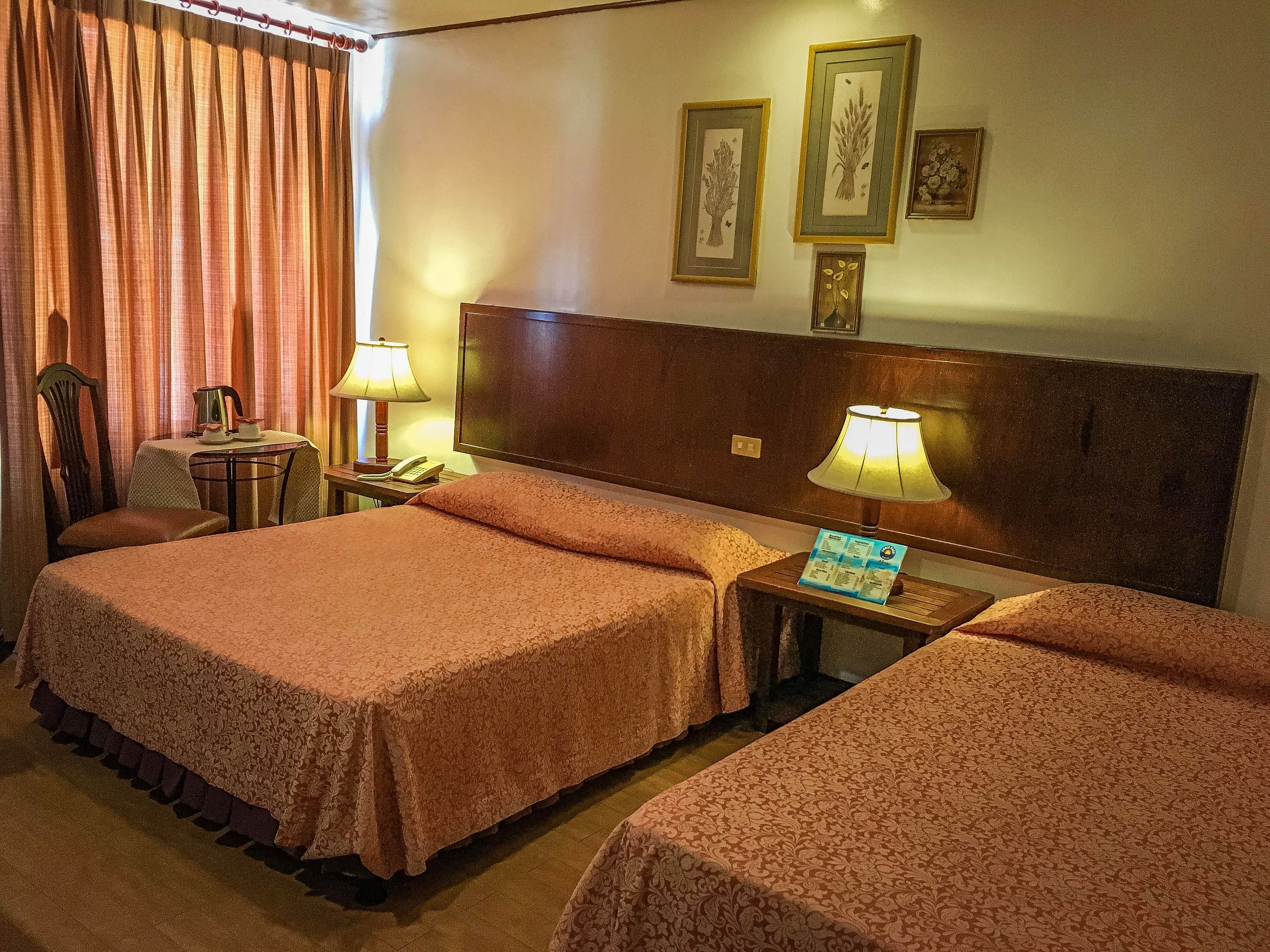 A hotel room with two beds, a desk, a chair, a lamp, and a telephone.