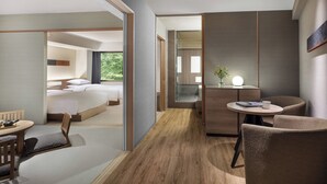 A modern hotel room with a wooden floor, a bed with white linens, a small round table with a lamp, and a seating area with chairs.