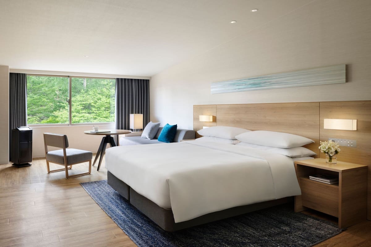 Habitación de hotel moderna con una cama grande, un escritorio, una silla y vistas al exterior.