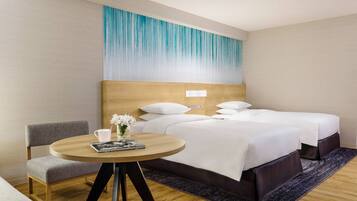 A hotel room with a bed, a bedside table with a lamp, a chair, and a wall with a blue gradient design.