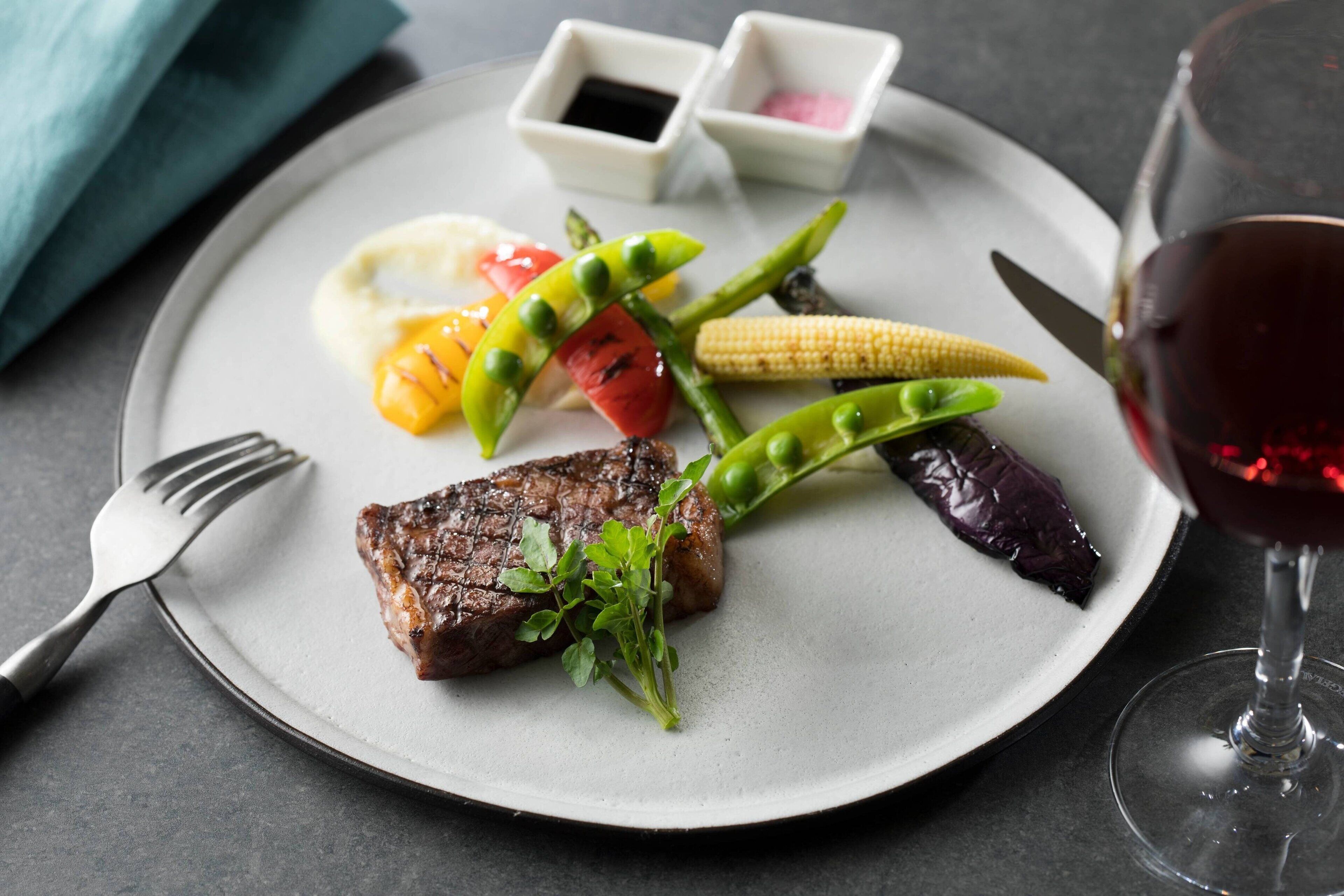 A plate with a steak, vegetables, and a glass of red wine.