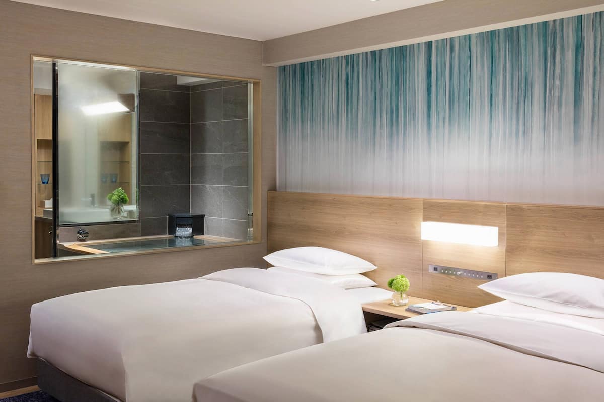 Habitación de hotel con dos camas, un espejo grande, un cabecero de madera y una lámpara fijada a la pared.