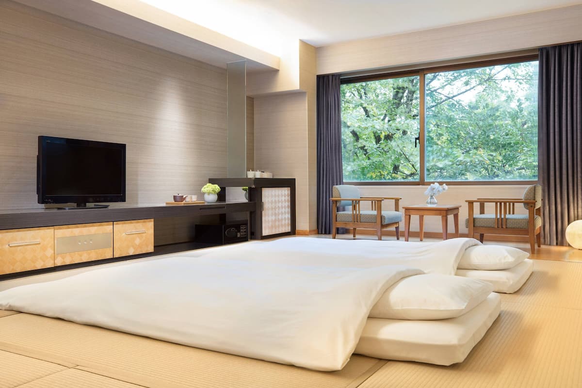 Una habitación de hotel moderna con una cama grande, televisión, escritorio y ventana con vista a árboles.
