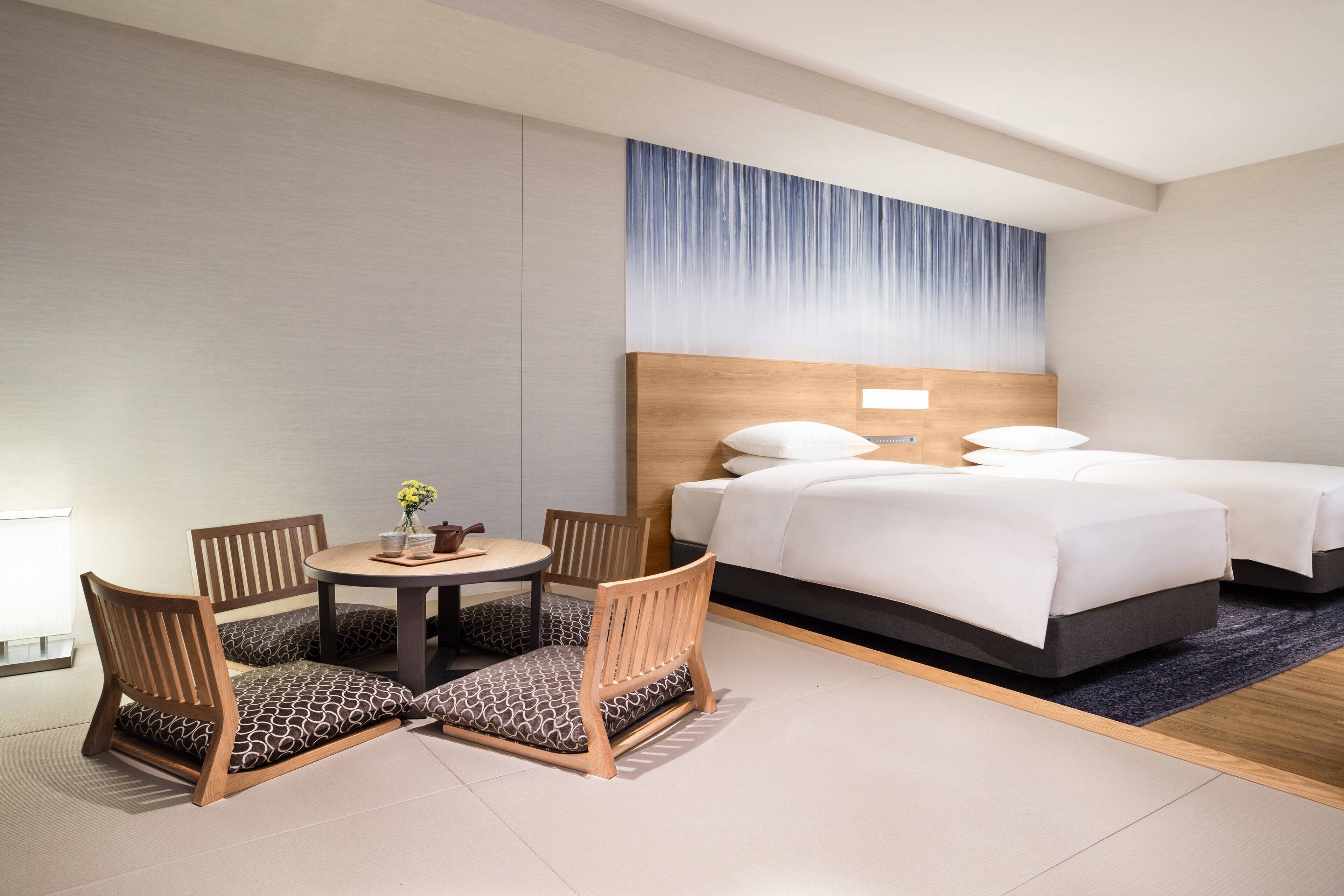 Una habitación de hotel con una cama, dos mesitas de noche, una mesa redonda con sillas y una pequeña mesa con un jarrón de flores.
