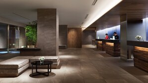 A modern lobby with a reception desk, seating area, and a large plant.