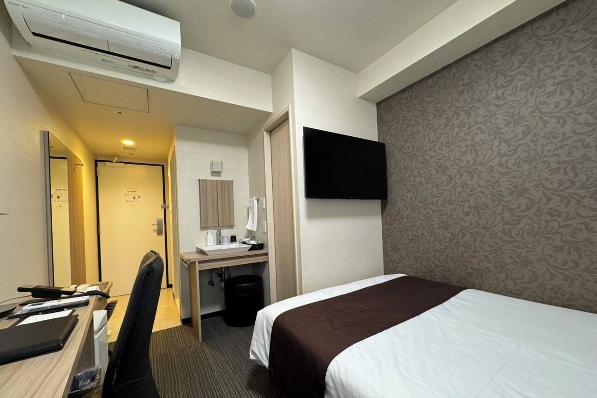 A hotel room with a bed, desk, chair, and a TV mounted on the wall.