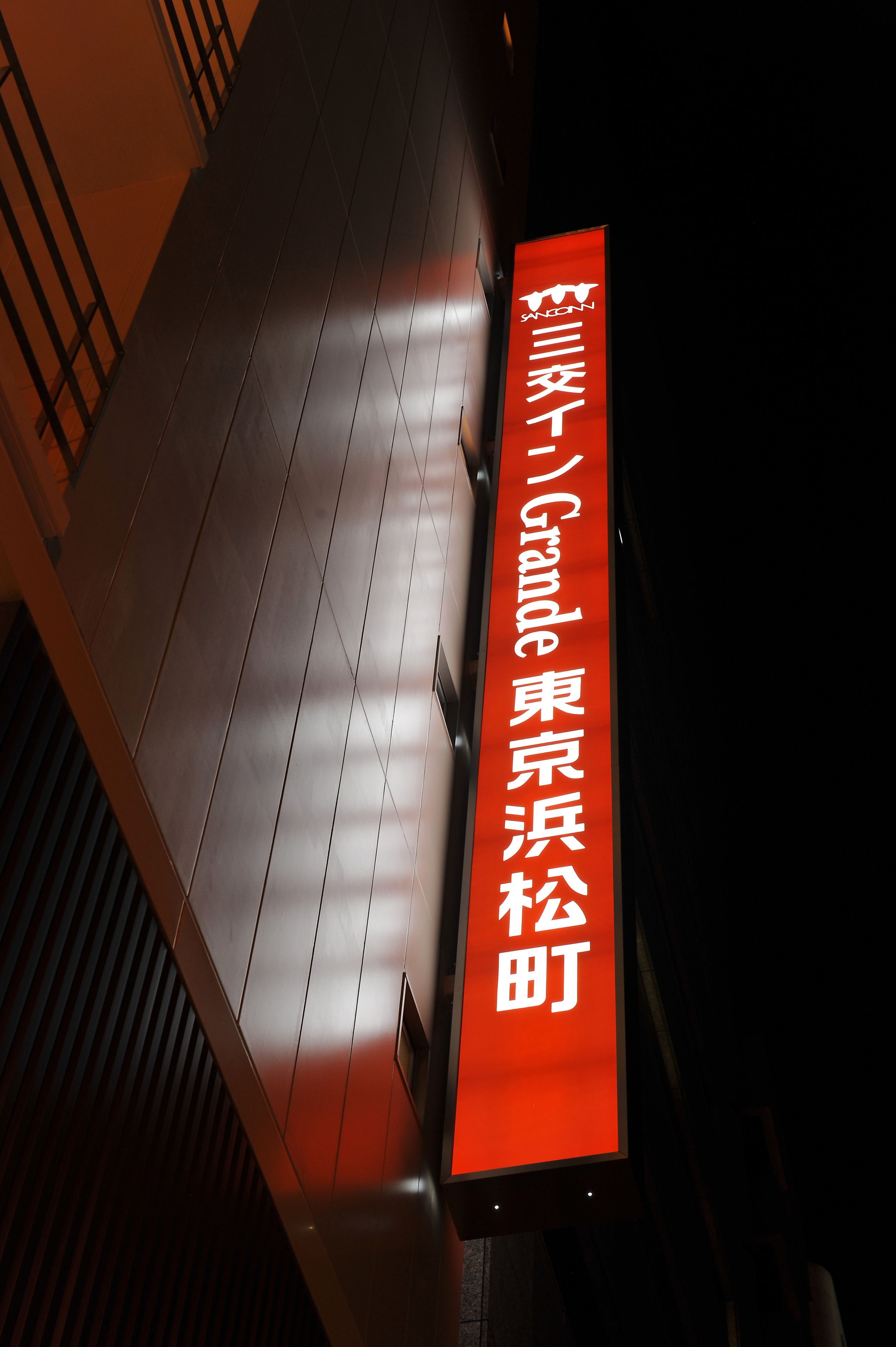 A red sign with white text on a building facade at night.